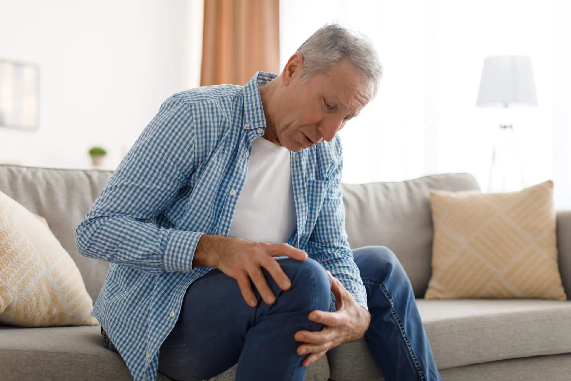 Why am I feeling hip and back pain after a total knee replacement? mature man with knee pain sitting on couch at home 2022 12 16 09 22 50 utc scaled Why am I feeling hip and back pain after a total knee replacement?